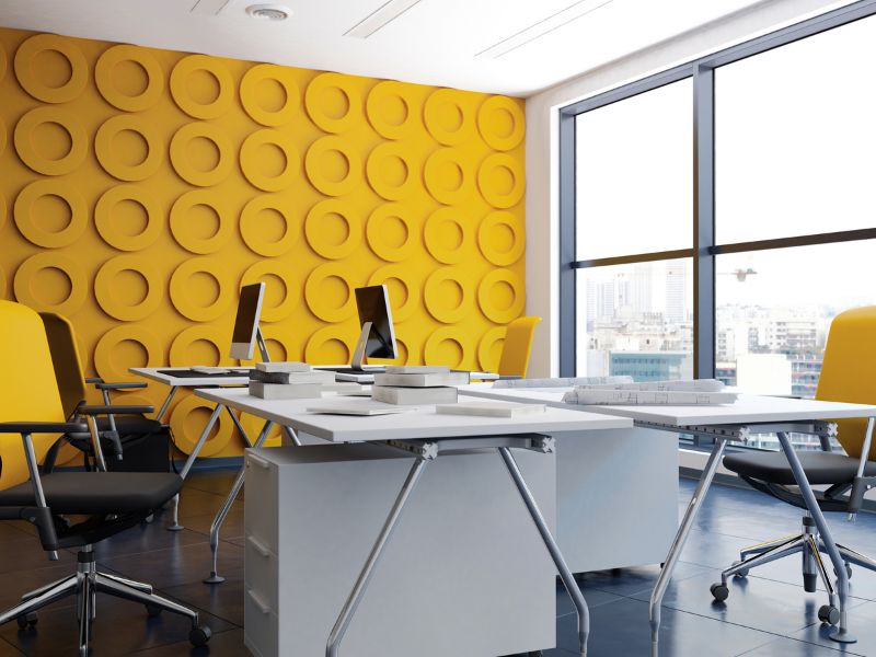 Moderno uređen radni prostor sa žutim zidom i crnim kancelarijskim stolicama kao primer upotrebe žute boje za kreativnost i optimizam.